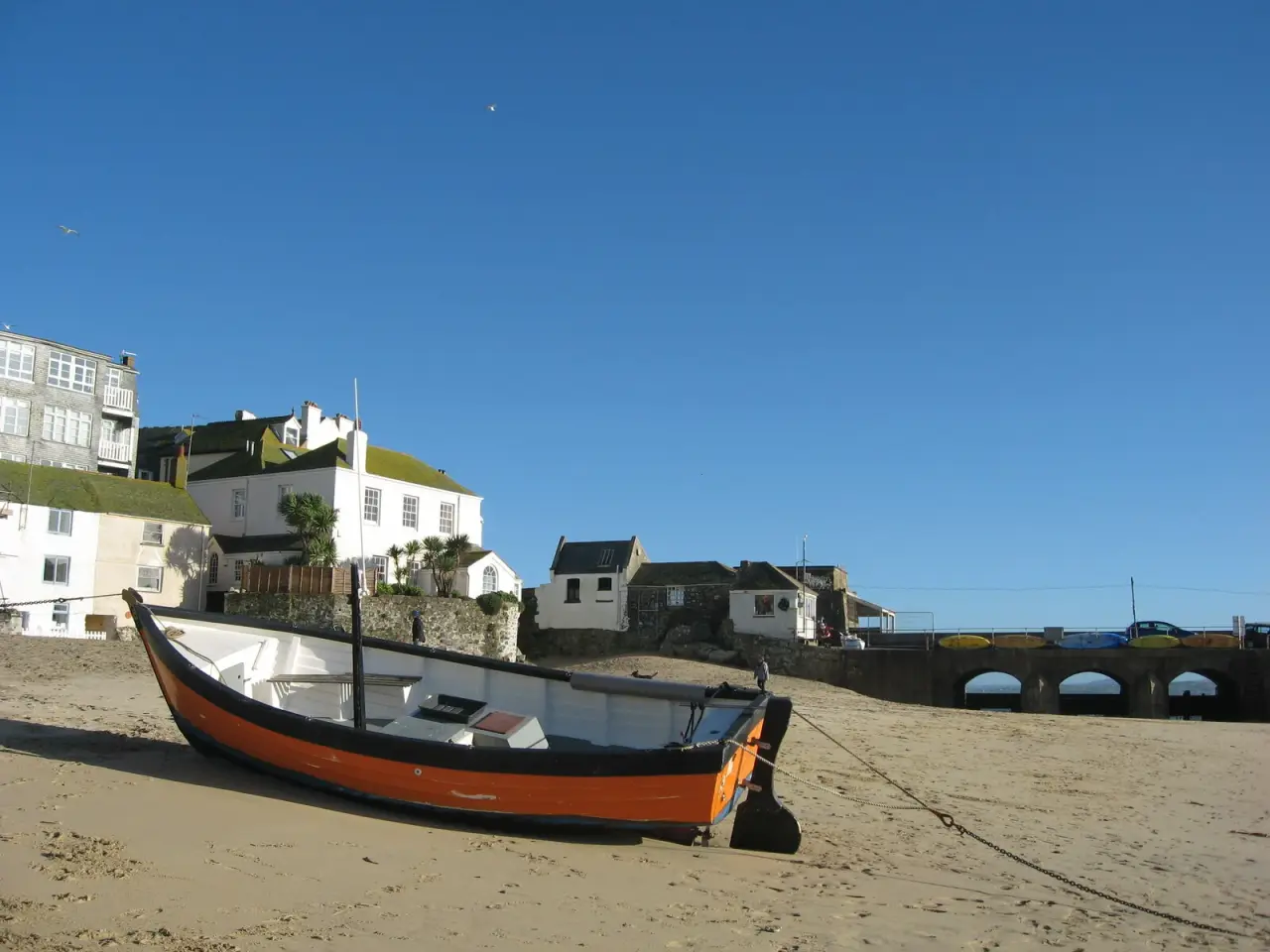Un barco naranja y negro en la arena en el puerto de St Ives bajo un cielo azul claro