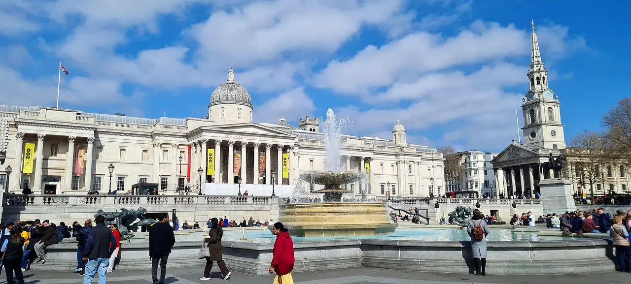 The National Gallery and a Trafalgar Square fountain beneath blue sky in London