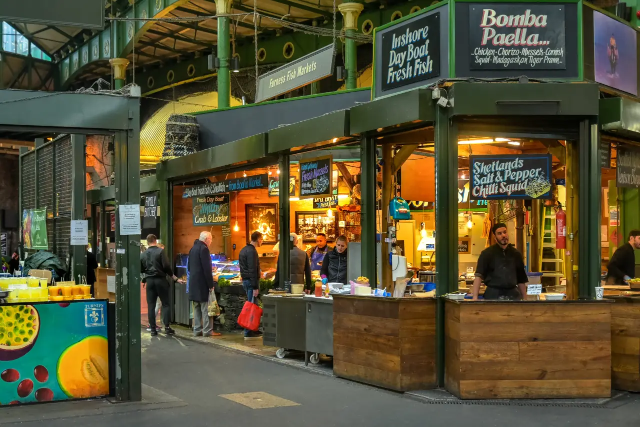 Comerciantes y visitantes junto a puestos de comida muy iluminados dentro de Borough Market, en Londres.
