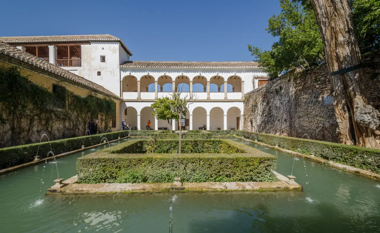 A sunlit garden courtyard and fountain pools beneath the white arcades of the Generalife in Granada.