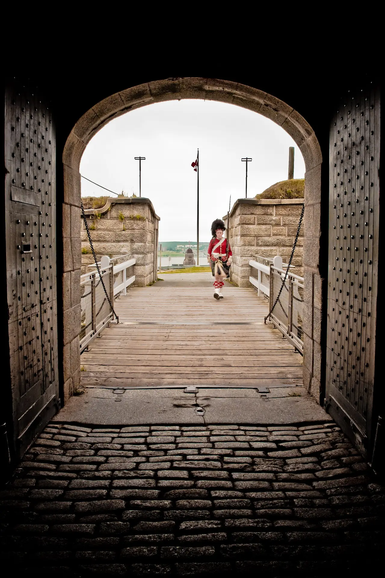 A historical interpreter in a red Highland uniform beyond the timber entrance of Halifax Citadel