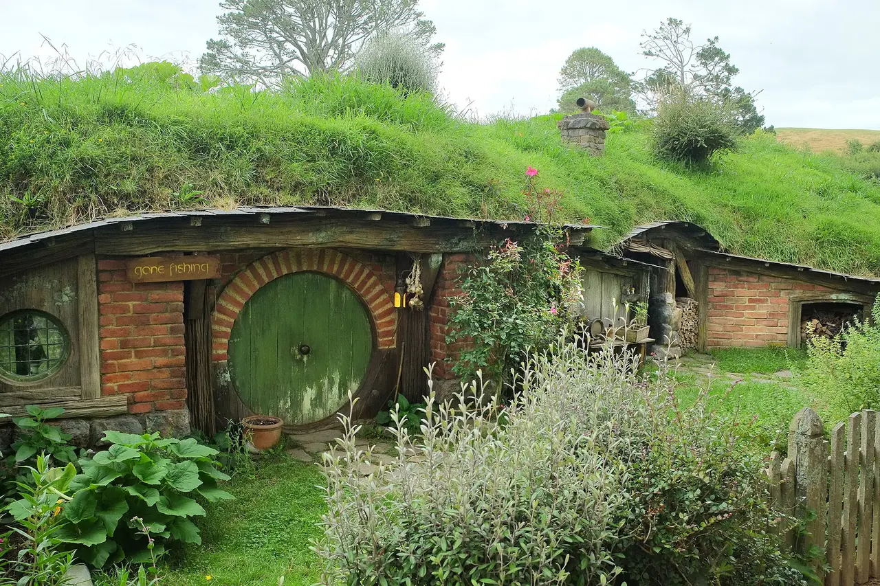 A round green door, red brickwork and fresh garden plants at Hobbiton Movie Set in New Zealand.