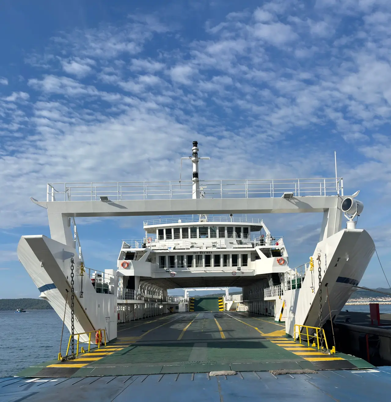 Rampa de proa abierta de un ferry y entrada a la cubierta de pasajeros bajo un cielo azul.