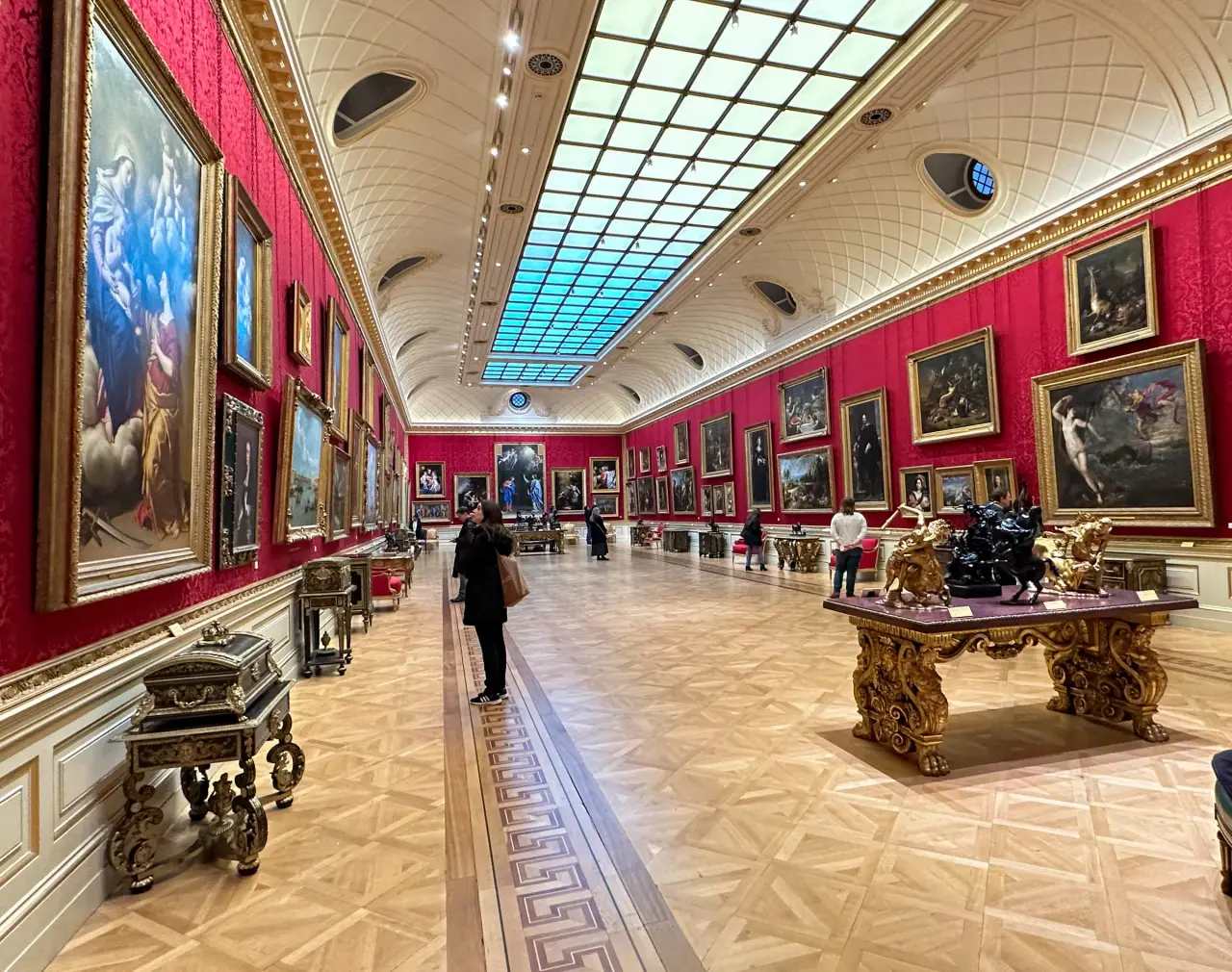 Besucher betrachten Gemälde und Kunsthandwerk in der rotwandigen Great Gallery der Wallace Collection in London.