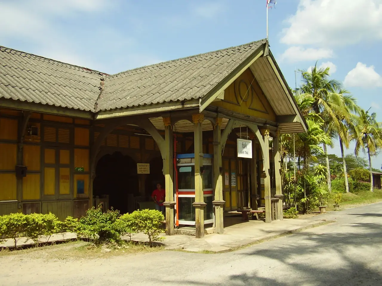 Yellow timber entrance of Kantang railway station with palm trees in daylight