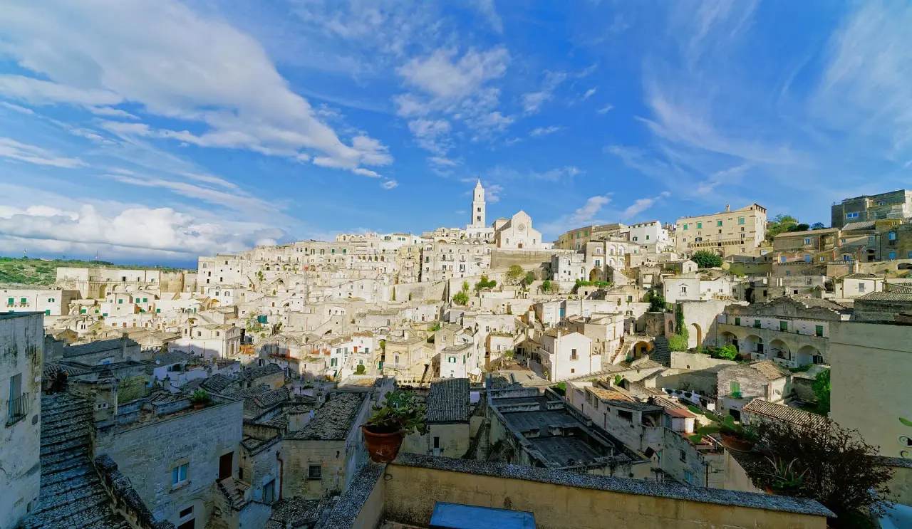 Sunlit stone houses of the Sassi in Matera beneath the cathedral and a blue sky