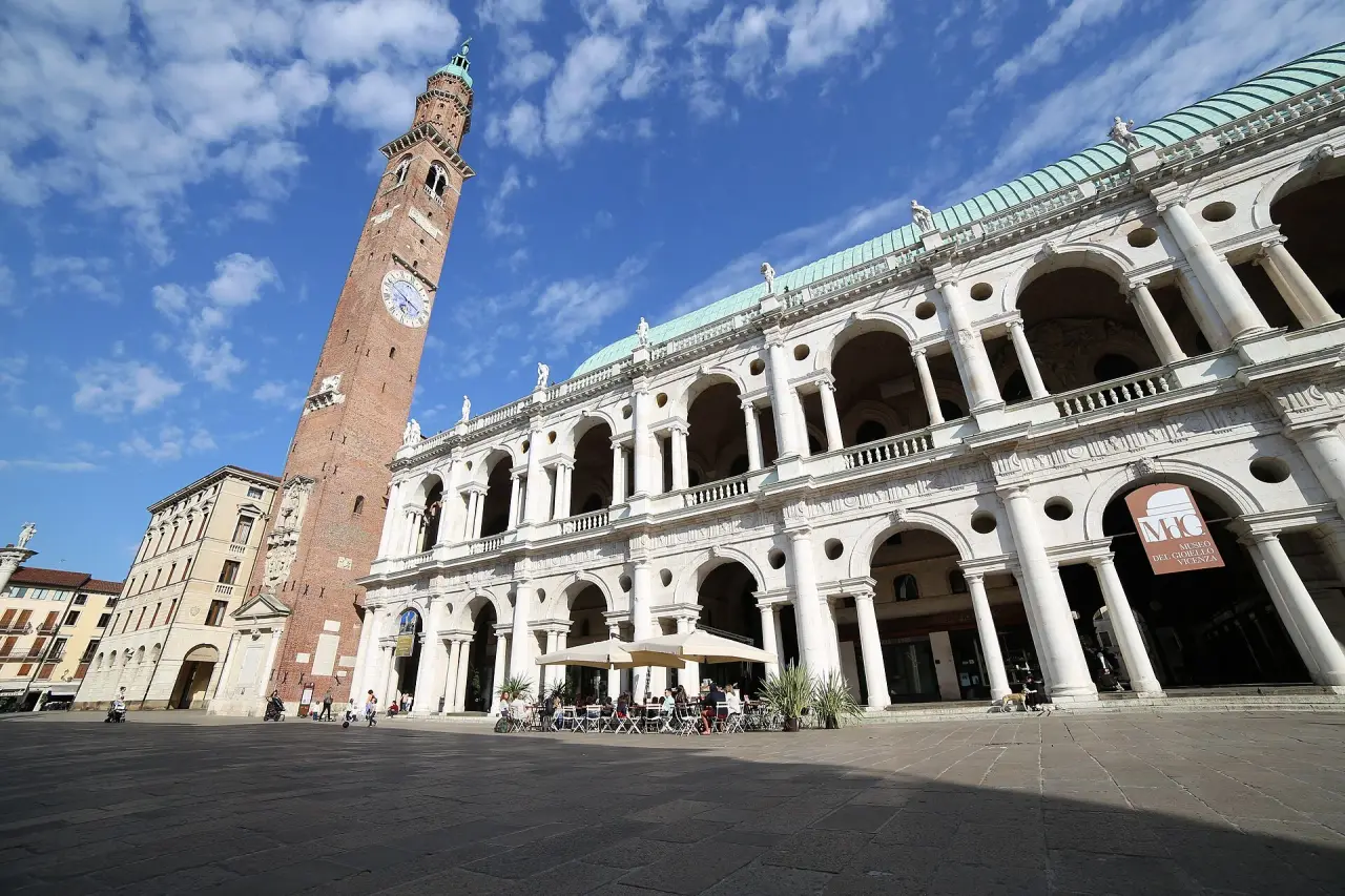 Basilica Palladiana สีขาวที่มีซุ้มโค้งและหอนาฬิกาอิฐใน Vicenza ใต้ท้องฟ้าสีฟ้า