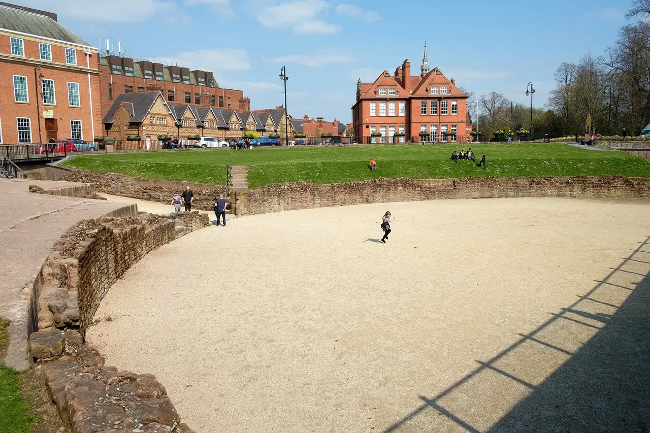 Visitors exploring the curved Roman amphitheatre remains in Chester on a bright day.