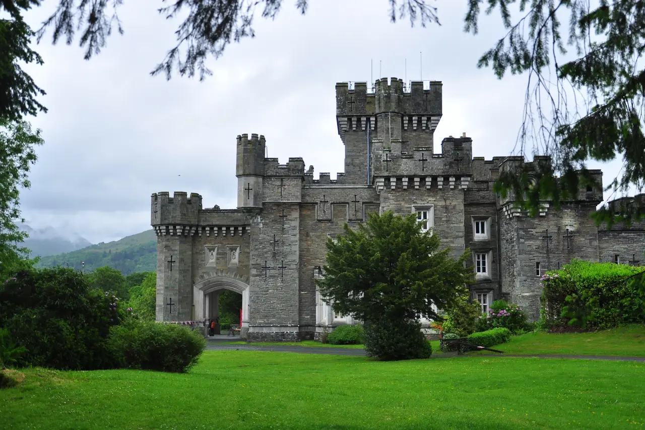 Stone towers of Wray Castle above a green lawn and shrubs in the Lake District.