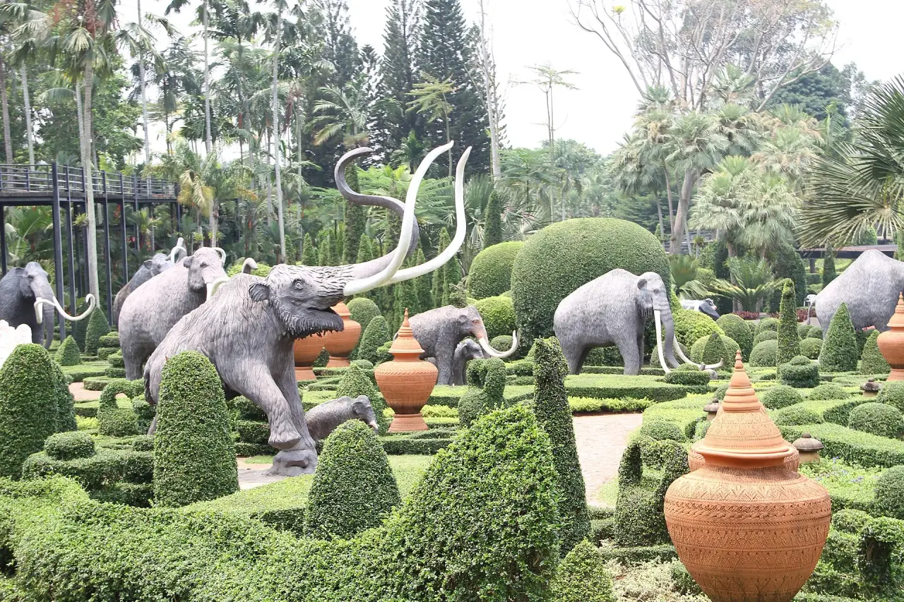 Mammoth sculptures among clipped green topiary, palms and terracotta pots at Nong Nooch Tropical Garden