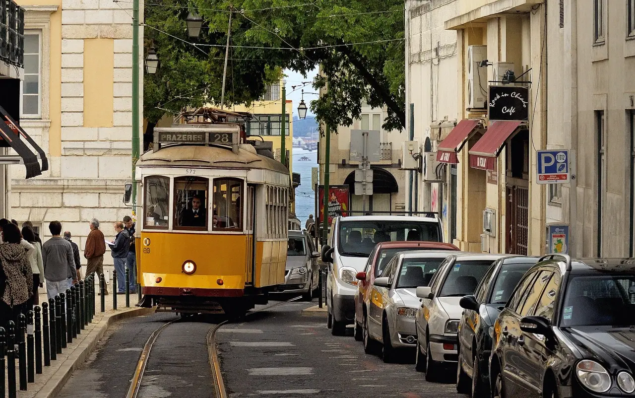 A yellow tram on a sunlit street in Lisbon with buildings and parked cars alongside