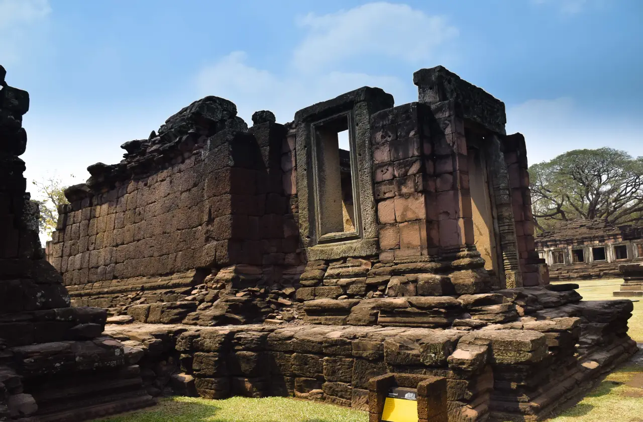 Sunlight falls on stone walls and a carved doorway at Phimai Historical Park under a blue sky.