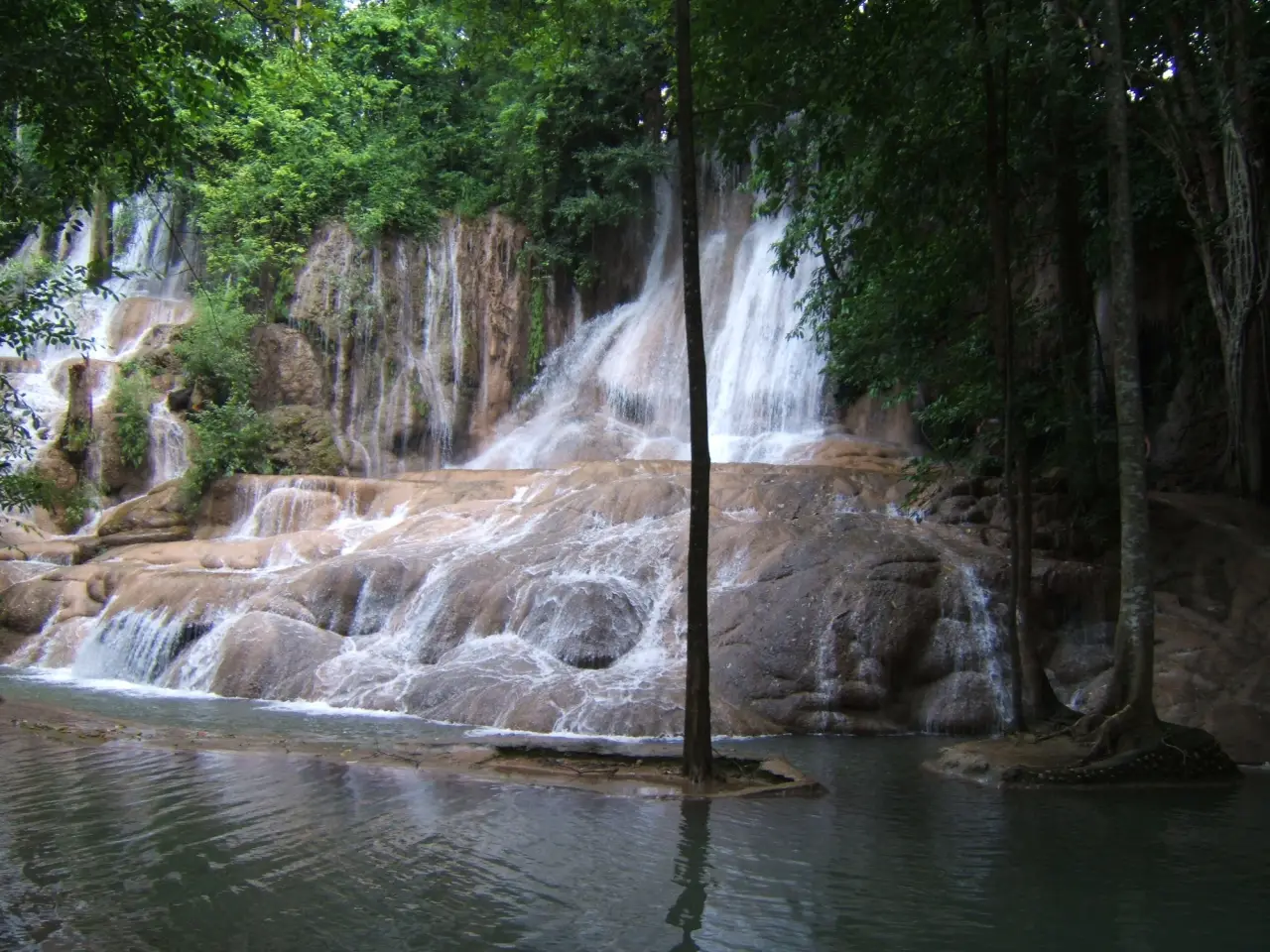 Sai Yok Noi Waterfall cascades over limestone beneath green forest in Kanchanaburi.