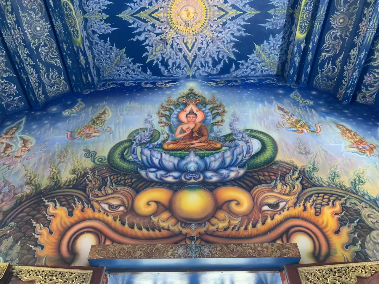 A blue-and-gold interior mural with a seated Buddha at Wat Rong Suea Ten in Chiang Rai.
