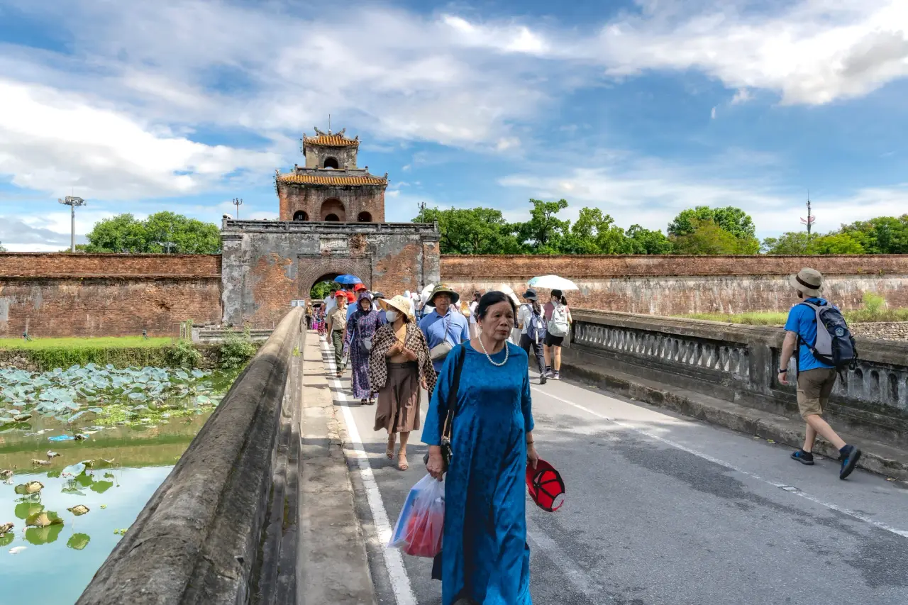 Visitors crossing a stone bridge towards an imperial citadel gate in Huế, Vietnam.