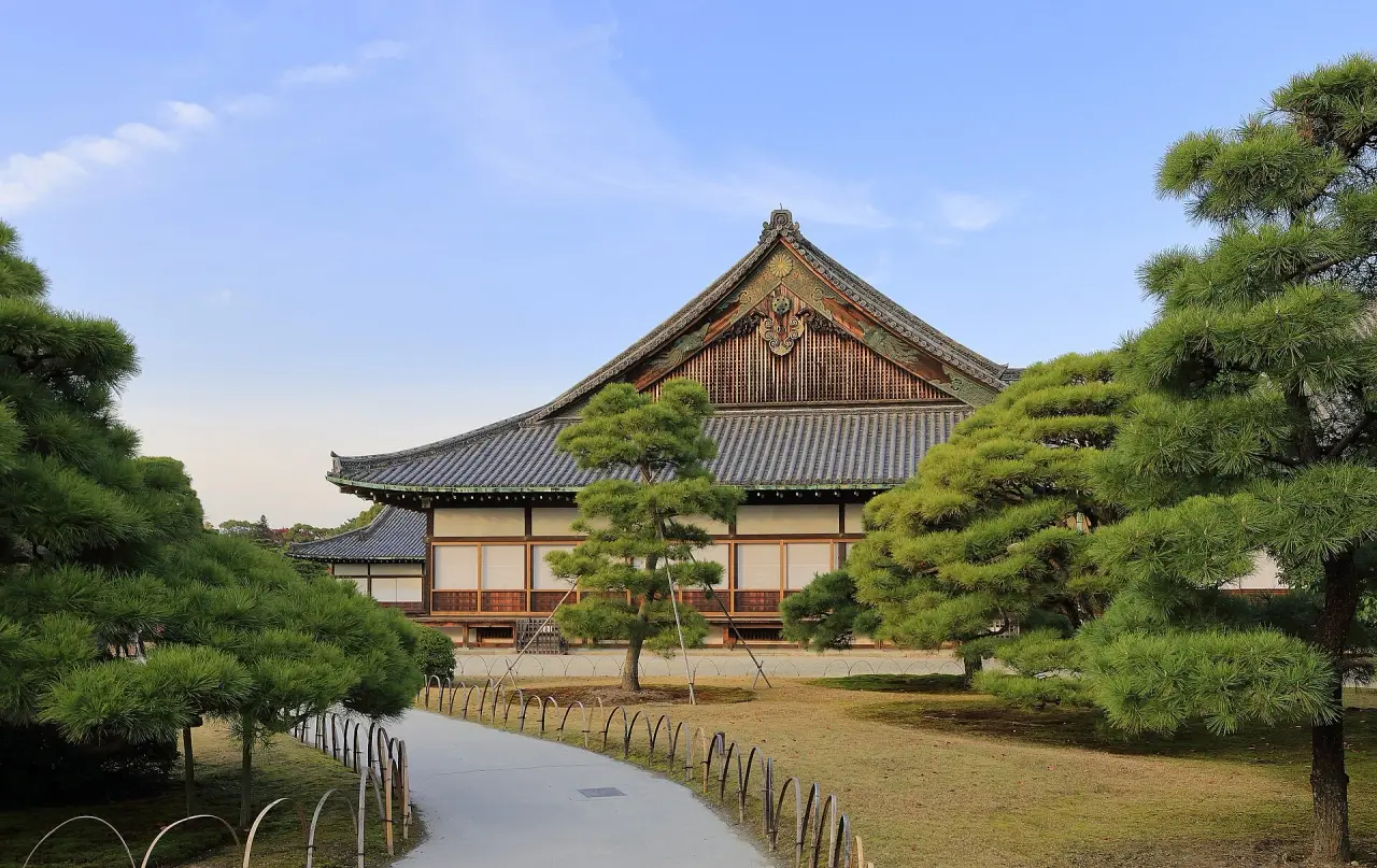 Ninomaru Palace at Nijo Castle framed by sculpted green pines beneath a blue sky in Kyoto.