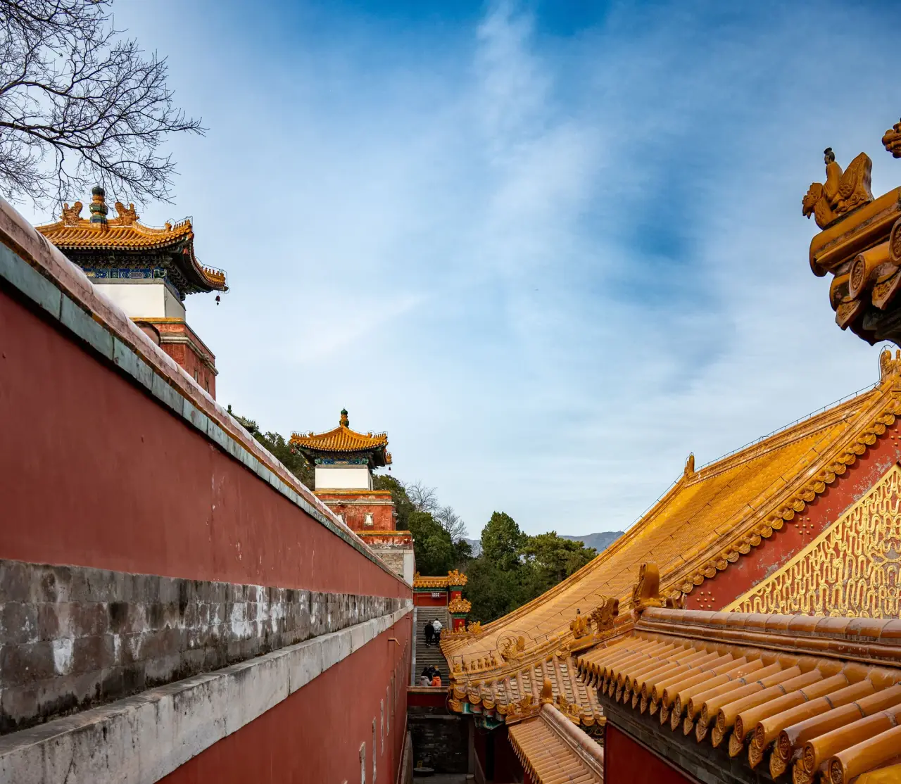Les tuiles de toit doré et les murs rouges encadrent un passage dans un temple chinois sous un ciel bleu et blanc.