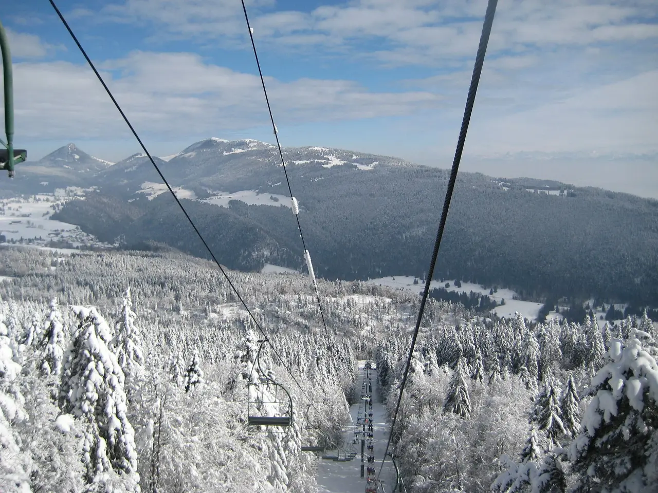 A chairlift above snow-covered trees and mountains in France