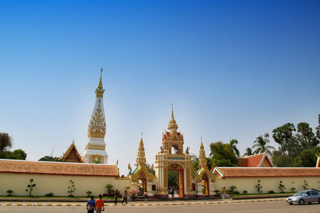 สถูปพระ That Phanom ขาวและสีทองหลังประตูวัดอันหรูหราภายใต้ท้องฟ้าสีคราม