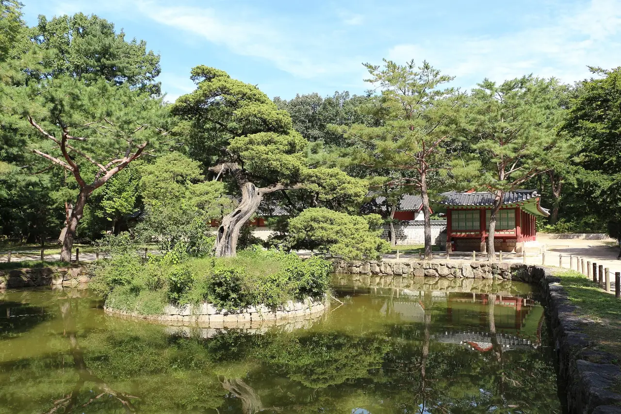 A small traditional pavilion beside a pond and green trees inside Jongmyo Shrine in Seoul.