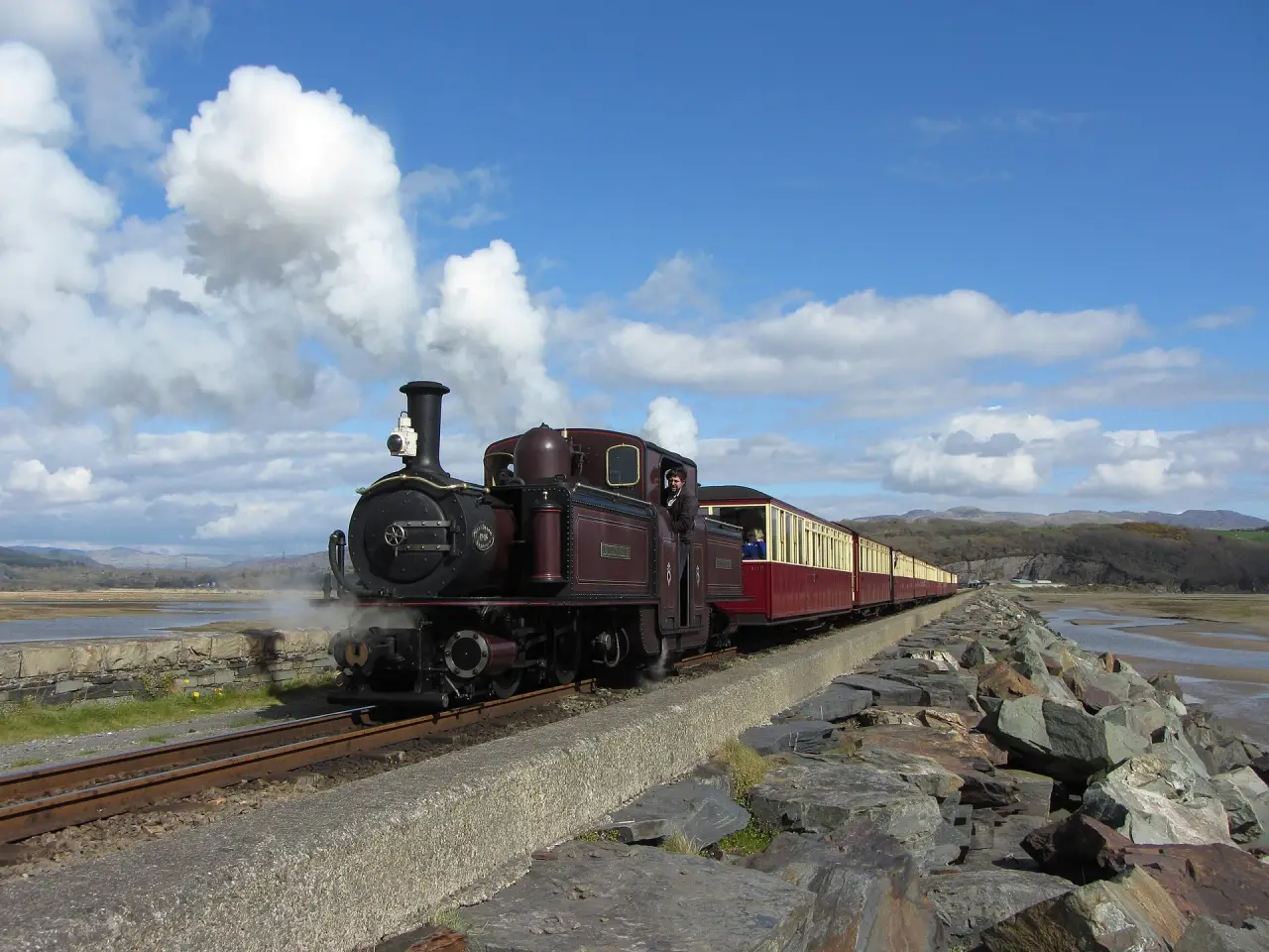 Un train Ffestinog Railway traversant le remblai Cob à côté de l'estuaire sous un ciel bleu vif