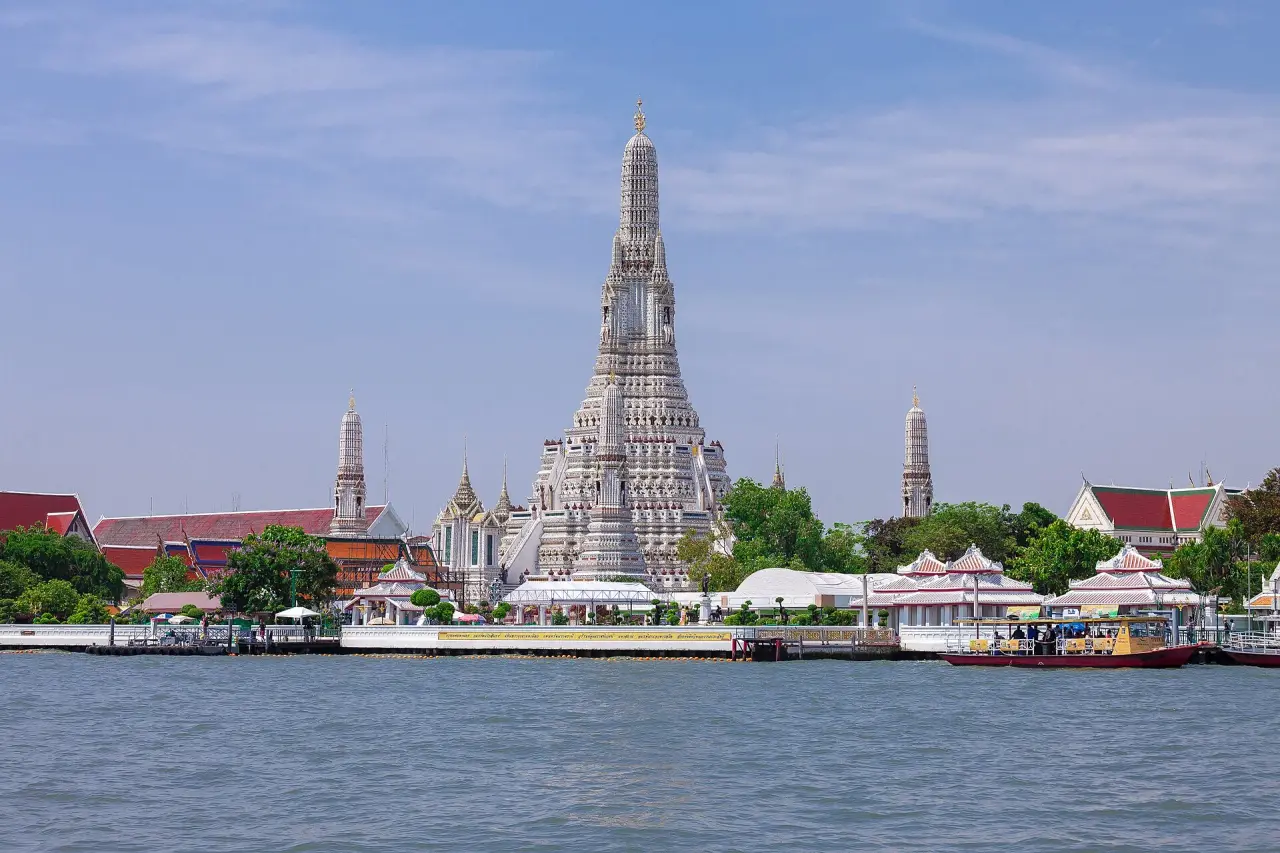 Wat Arun central prang and riverside temple grounds seen across the Chao Phraya in daylight