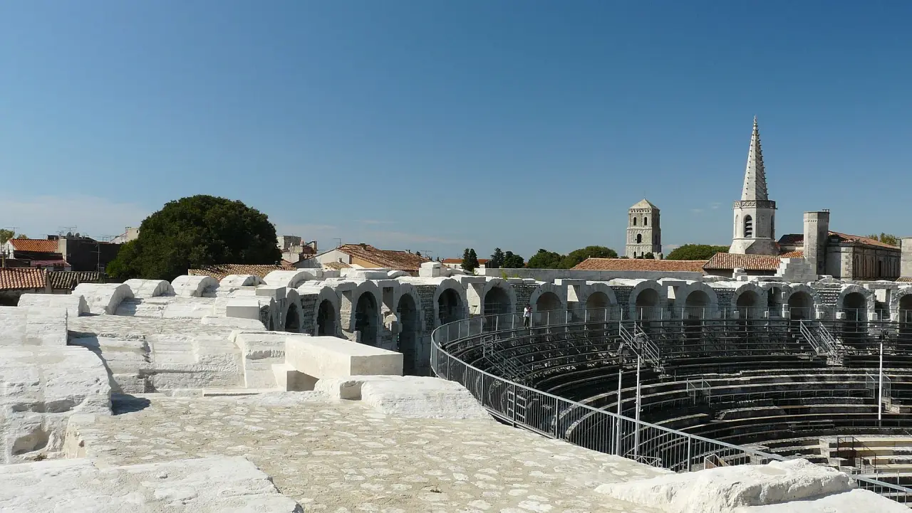 Sunlit limestone arches and seating inside the Roman amphitheatre in Arles beneath a blue sky