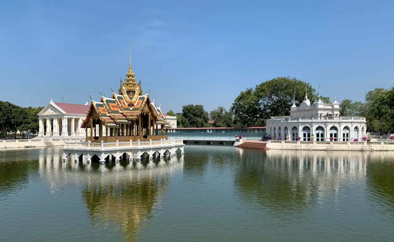 Le pavillon doré Aisawan Thiphya-At se dresse au-dessus d’un bassin du palais de Bang Pa-In, avec un ciel bleu et des arbres verts en arrière-plan.