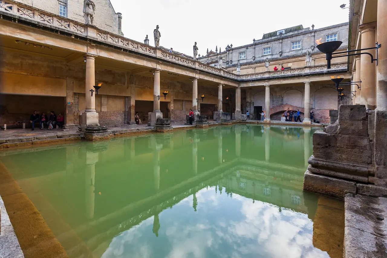 Agua termal verde y reflejos en el Gran Baño, enmarcados por las columnatas de piedra de tonos cálidos de las termas romanas de Bath