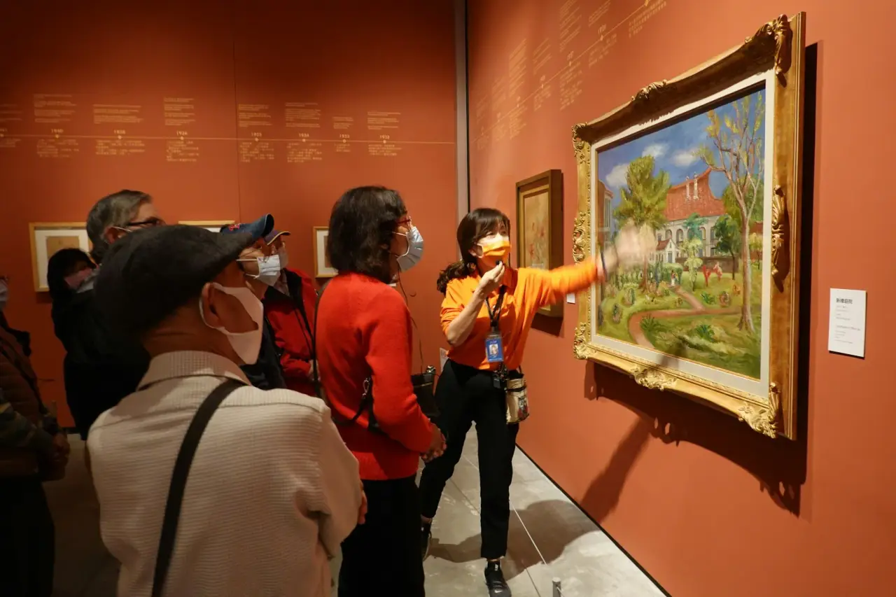 A museum guide pointing towards a framed painting beside visitors