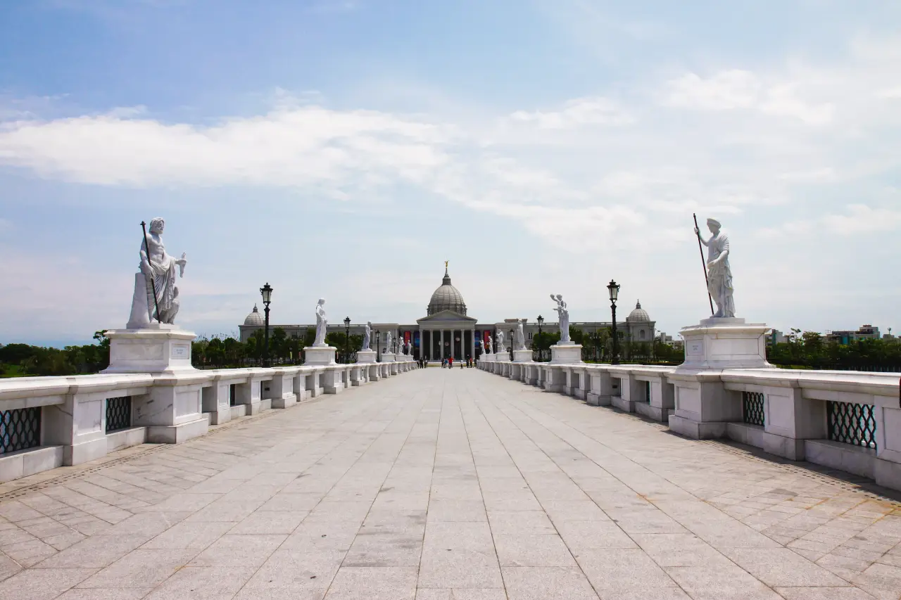 Ein von Statuen gesäumter Steinweg führt zum Chimei Museum mit seiner Kuppel in Tainan unter einem blau-weißen Himmel.