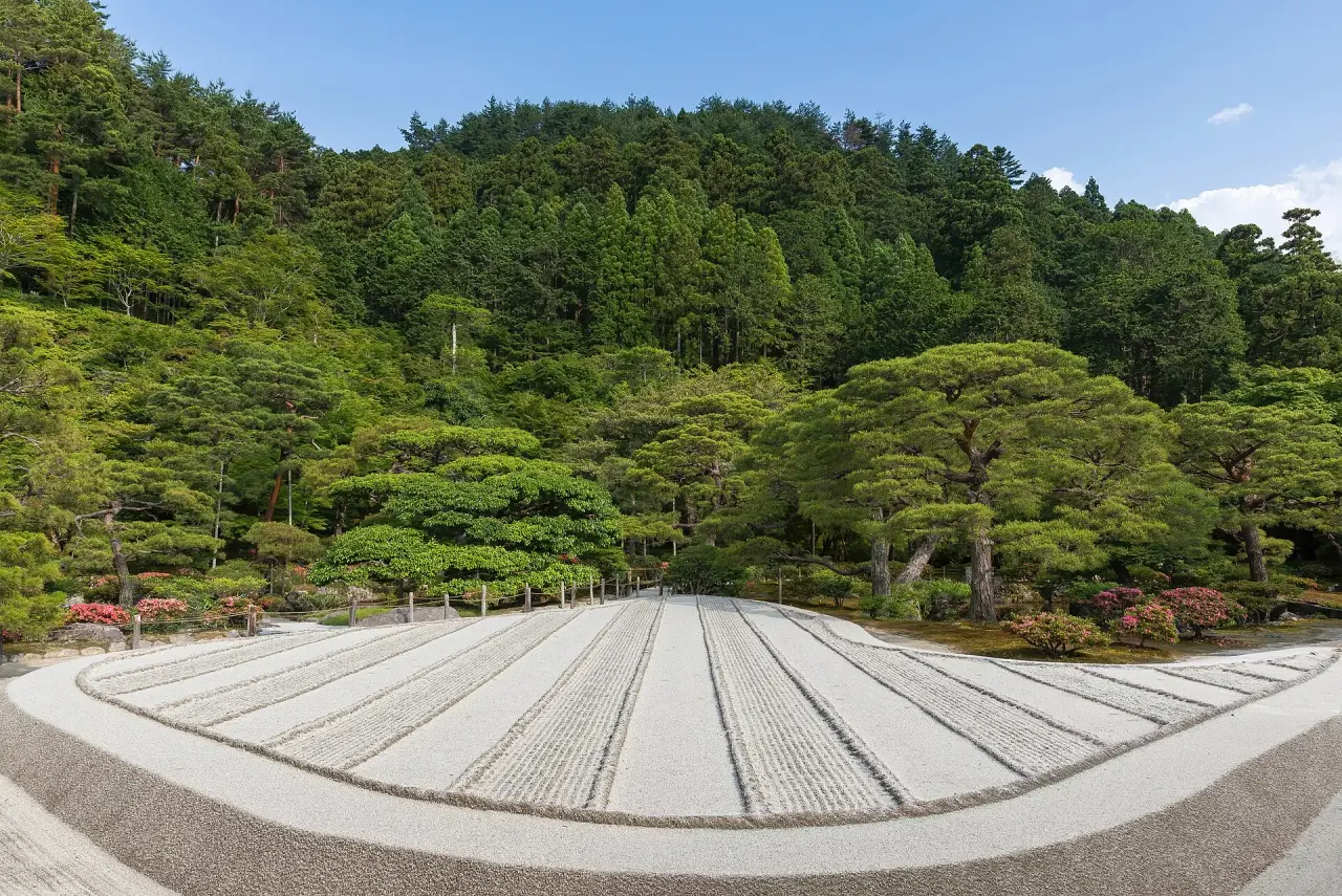 Raked pale sand and green pines in the garden of Ginkaku-ji in Kyoto on a sunny day