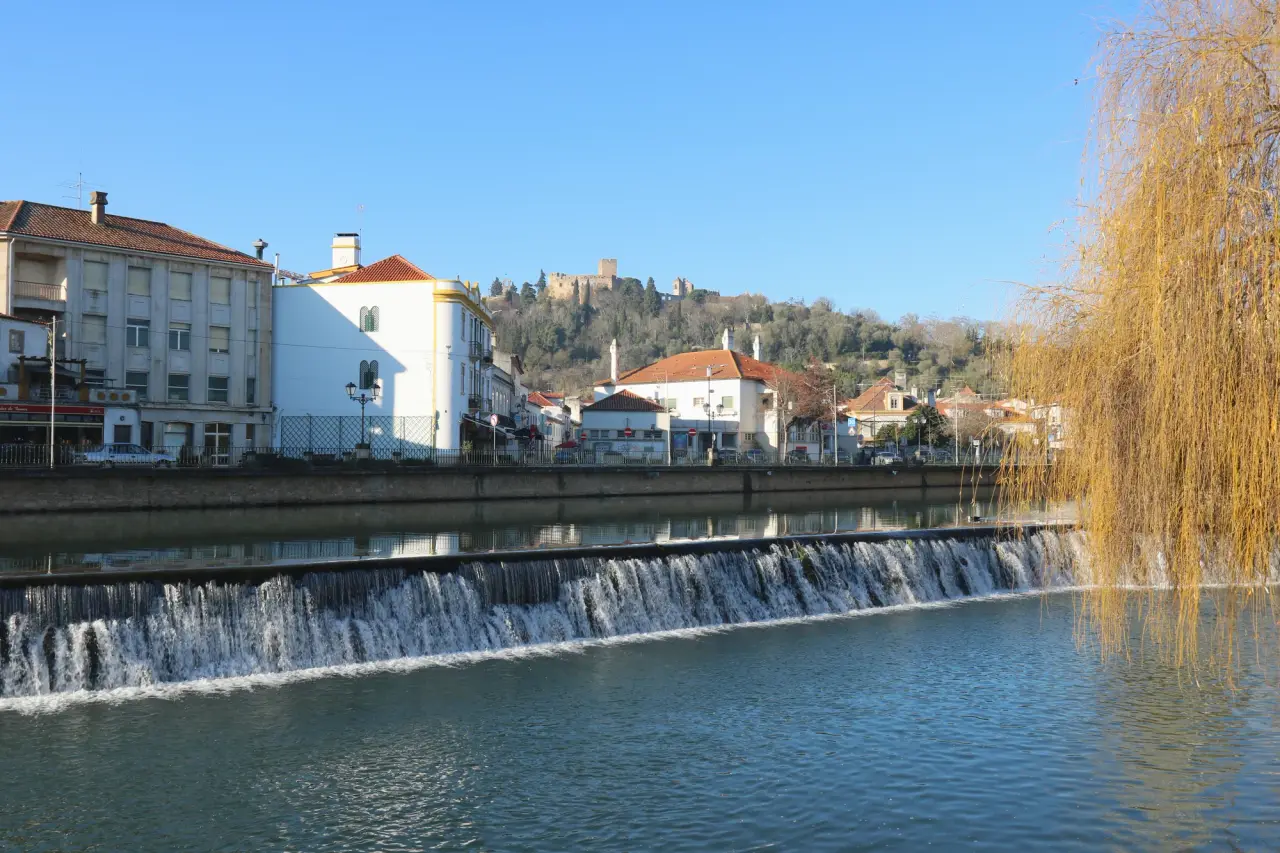 A low weir on the Nabão River with Tomar buildings and the castle on the hillside.