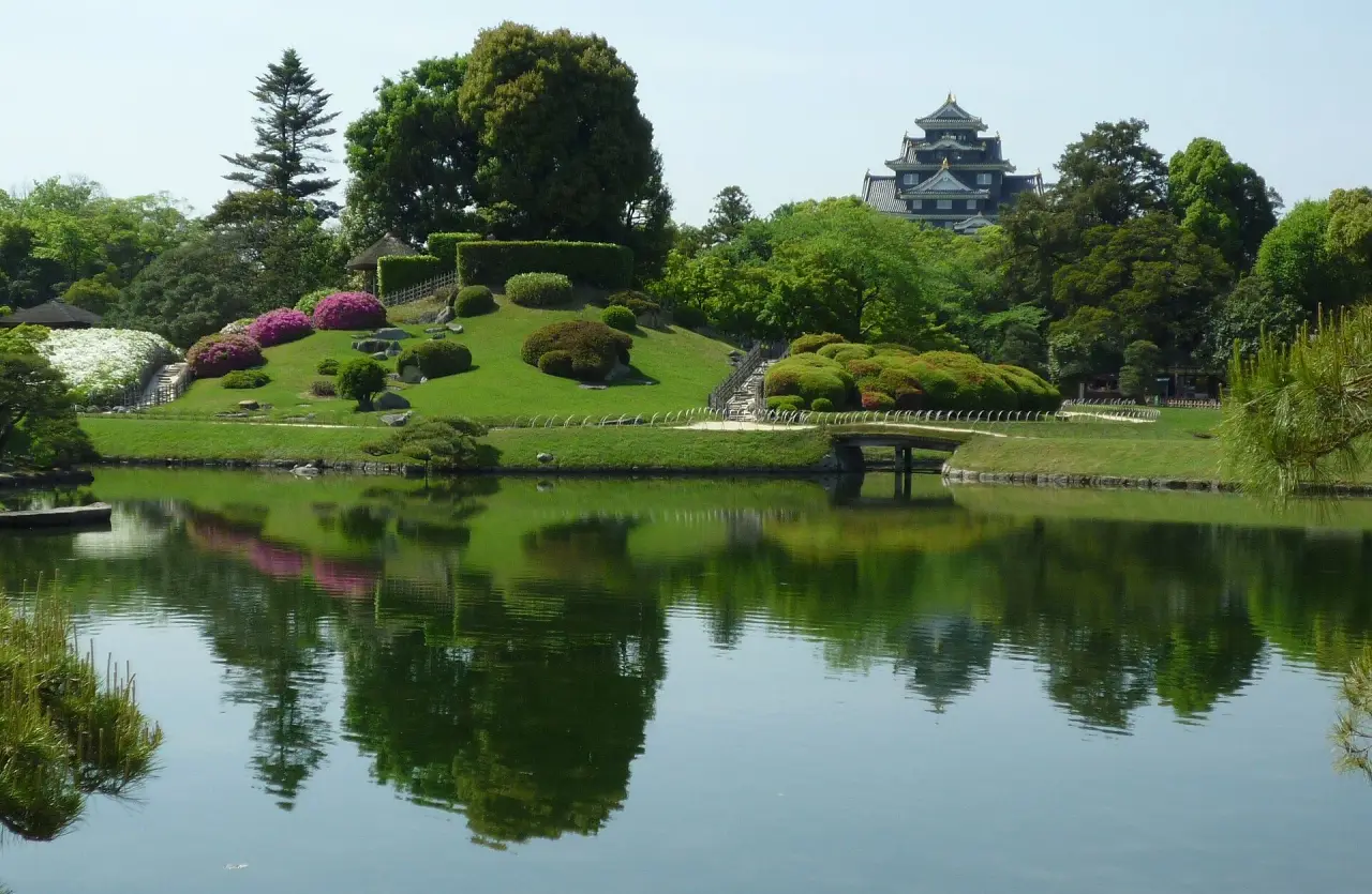 Fresh green planting, flowering shrubs and reflective Sawanoike Pond with Okayama Castle in the background at Korakuen.