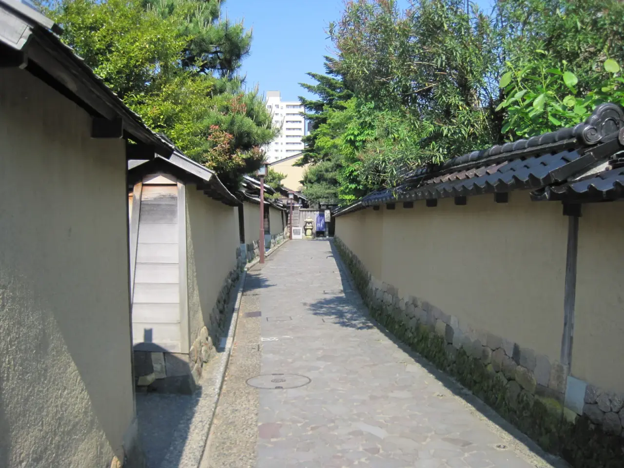 A sunny narrow lane between earthen walls in Nagamachi, Kanazawa