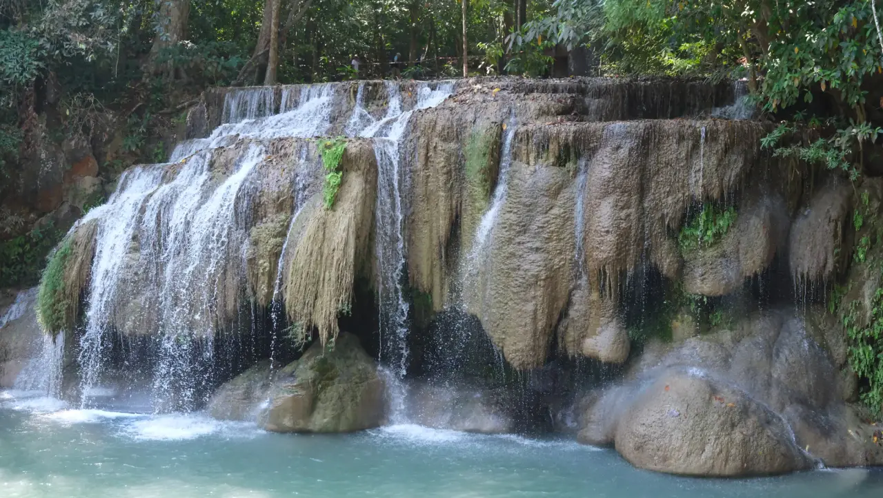 A limestone waterfall flows into a blue-green pool in Erawan National Park.