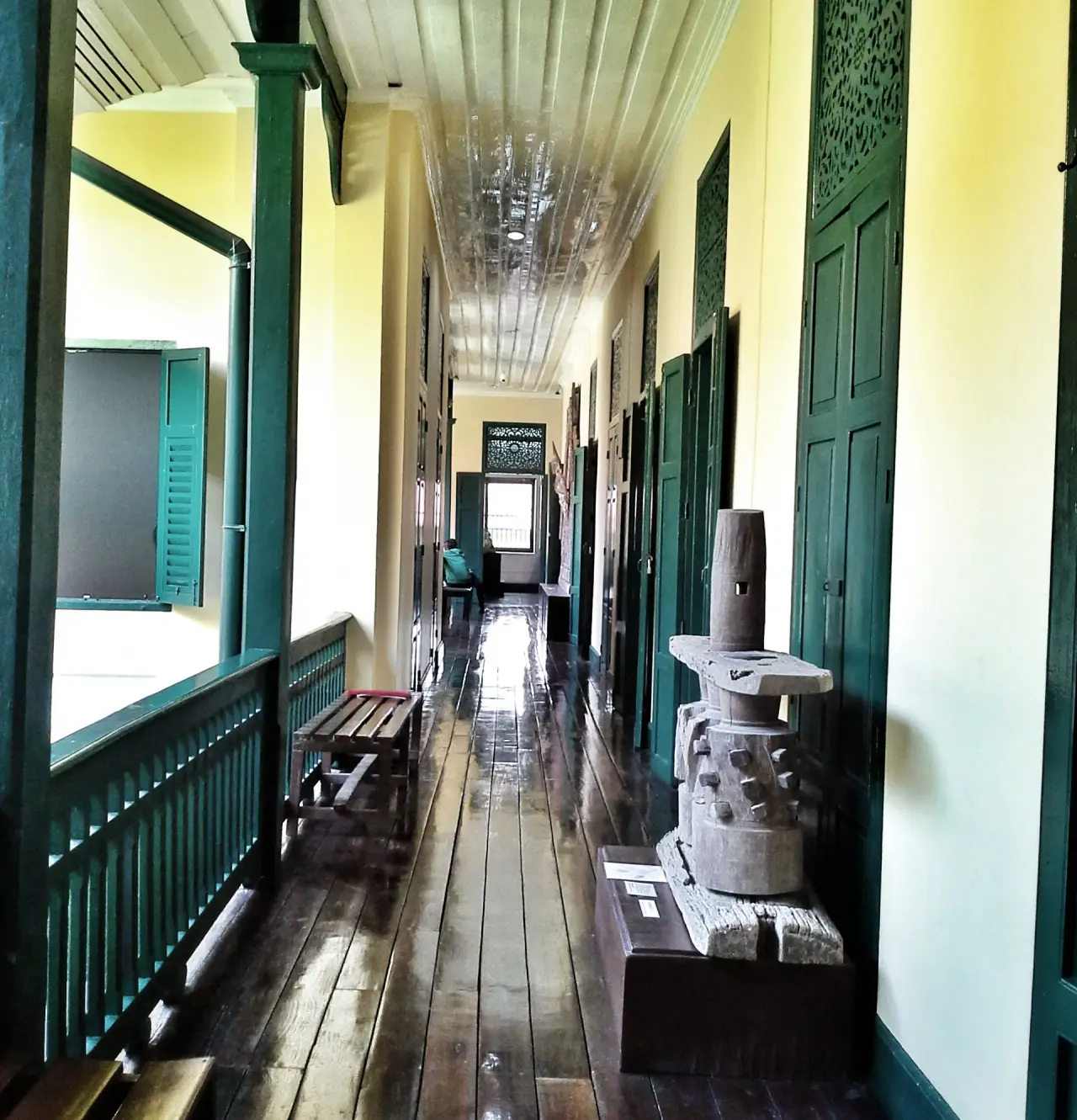 A naturally lit corridor with green shutters, cream walls and stone exhibits inside Ubon Ratchathani National Museum.
