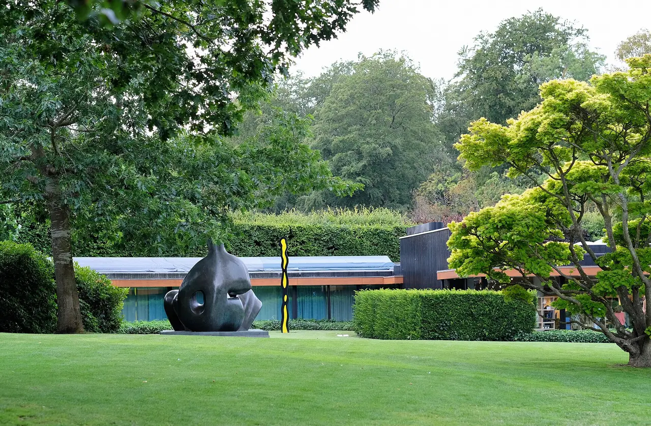 An outdoor sculpture on green lawns beside the low gallery buildings of Louisiana Museum of Modern Art