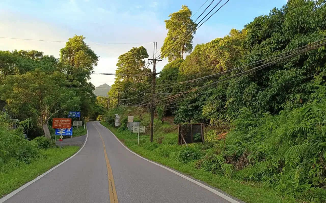 A sunlit road through lush green hills on Koh Chang