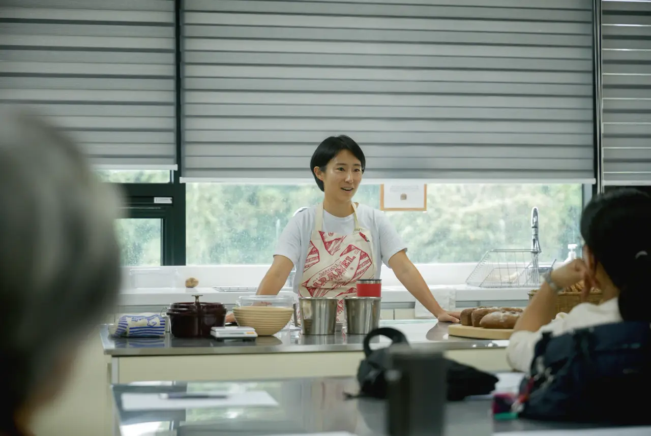 A cooking instructor demonstrates a preparation step to participants in a bright teaching kitchen.