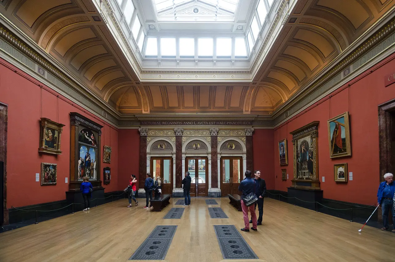 Visitors in the warm red galleries of the National Gallery Central Hall in London