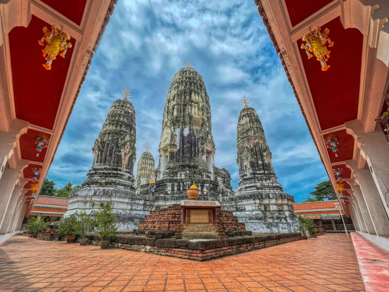 Stone prangs of Wat Mahathat Worawihan framed by a red-roofed cloister in Ratchaburi