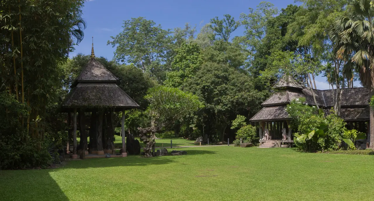 A timber pavilion stands beside a green lawn and tropical trees at Mae Fah Luang Art and Cultural Park in Chiang Rai.