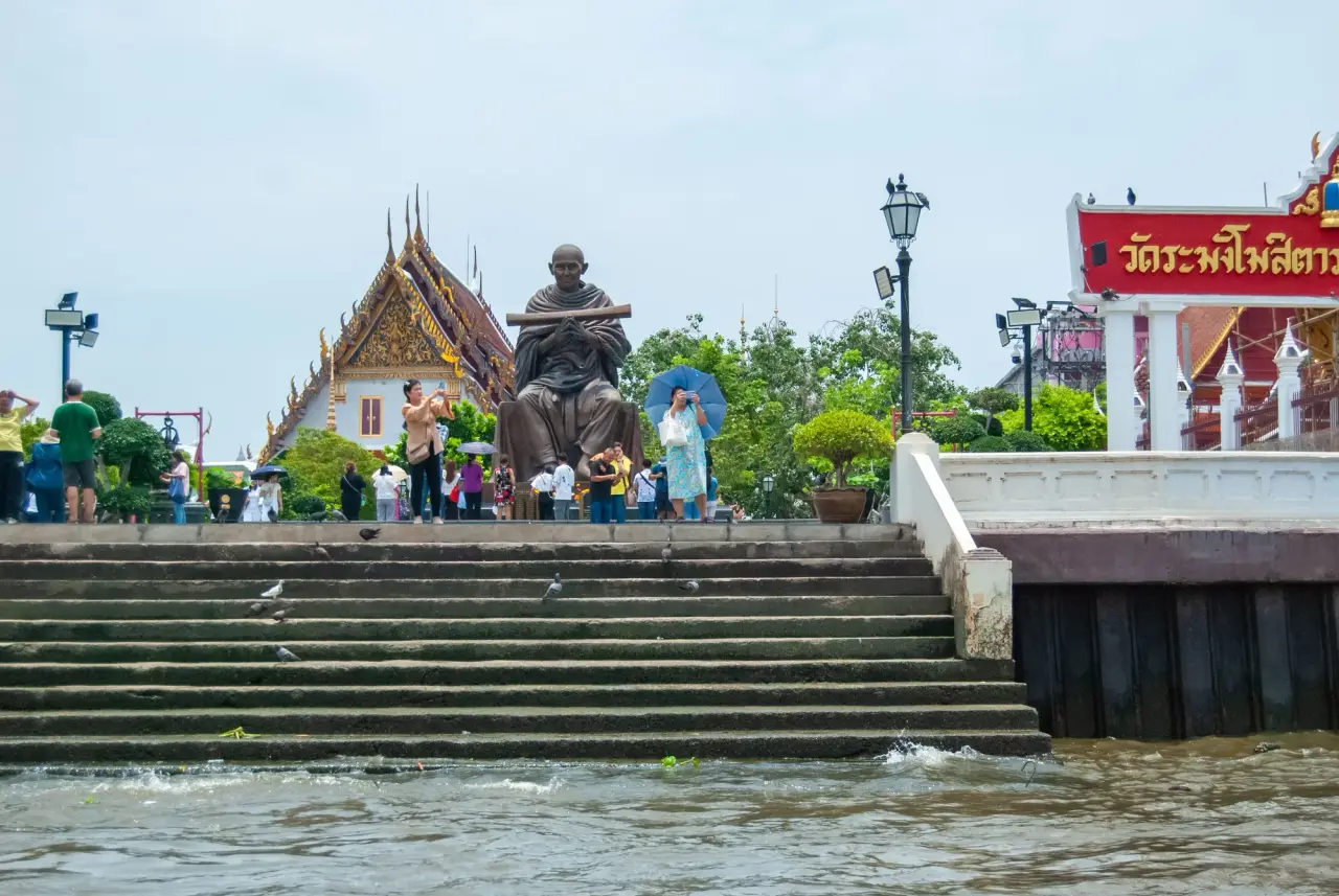 Stone steps rise from the waterfront to a temple courtyard with visitors and a seated statue.