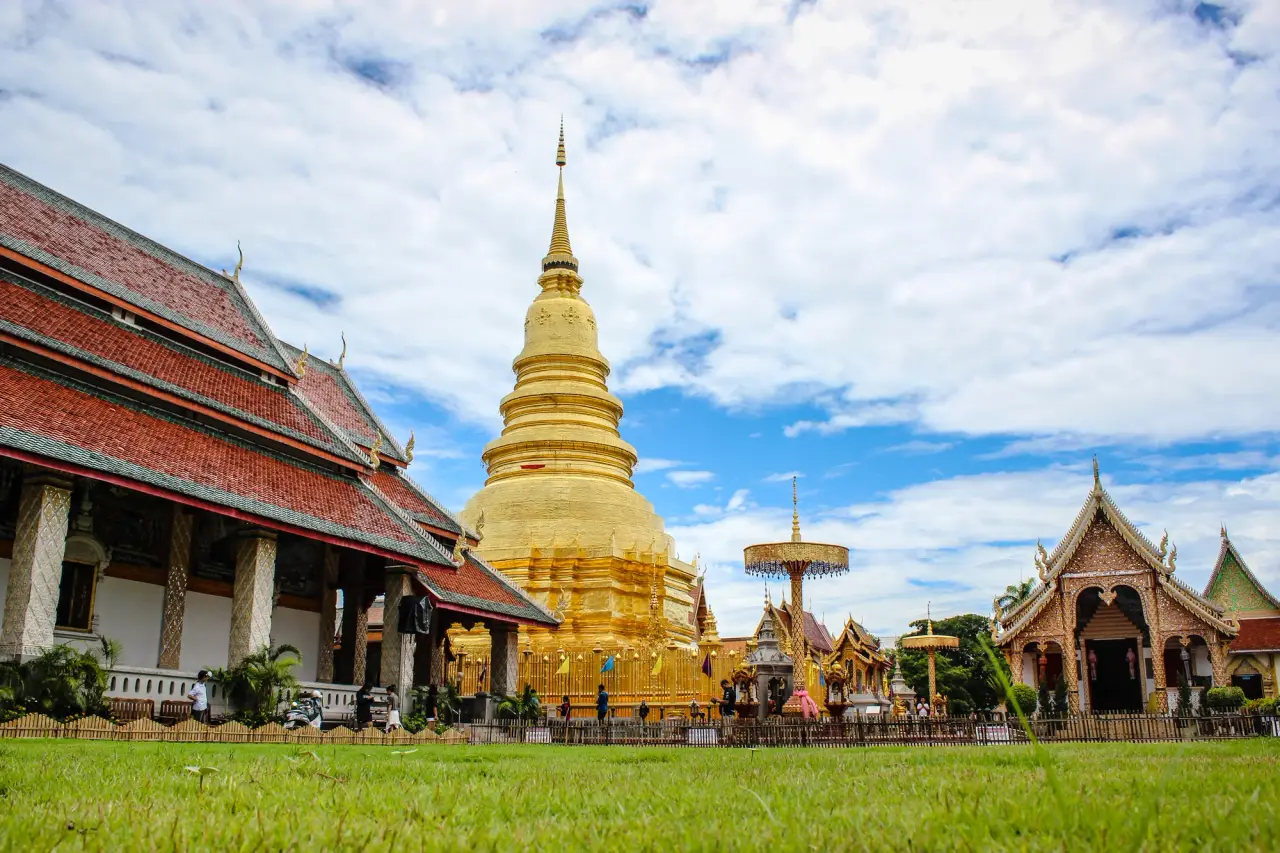 Stupa d'or de Wat Phra That Hariphunchai à côté des halls du temple et une pelouse verte à Lamphun