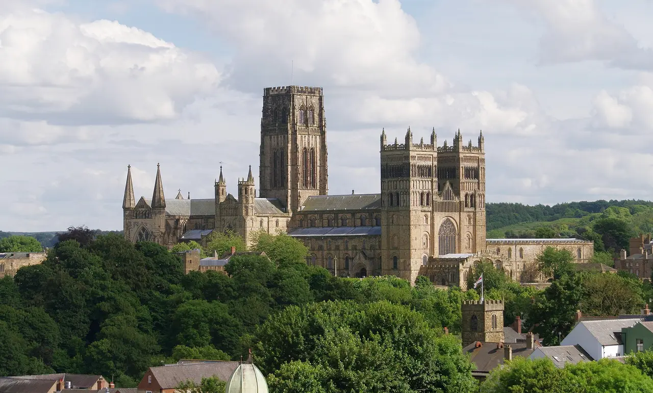 The complete main towers of Durham Cathedral rising above green riverside slopes