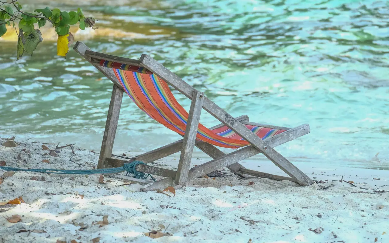 A colourful beach chair beneath palms beside the clear sea on Koh Samet