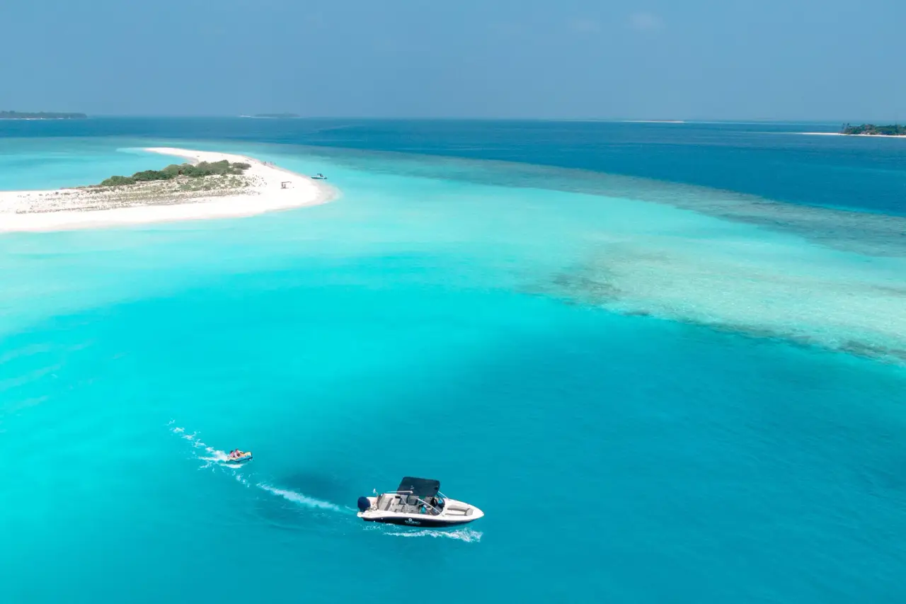 A small white motorboat crossing a turquoise lagoon beside a white-sand island.