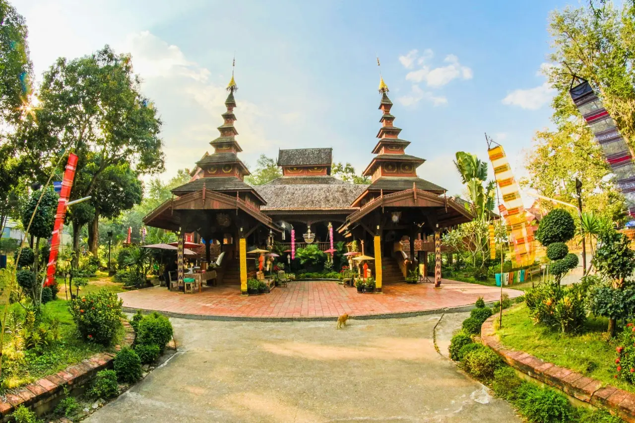 Wat Jom Sawan’s timber halls and tiered spires beyond the sunny entrance garden in Phrae.