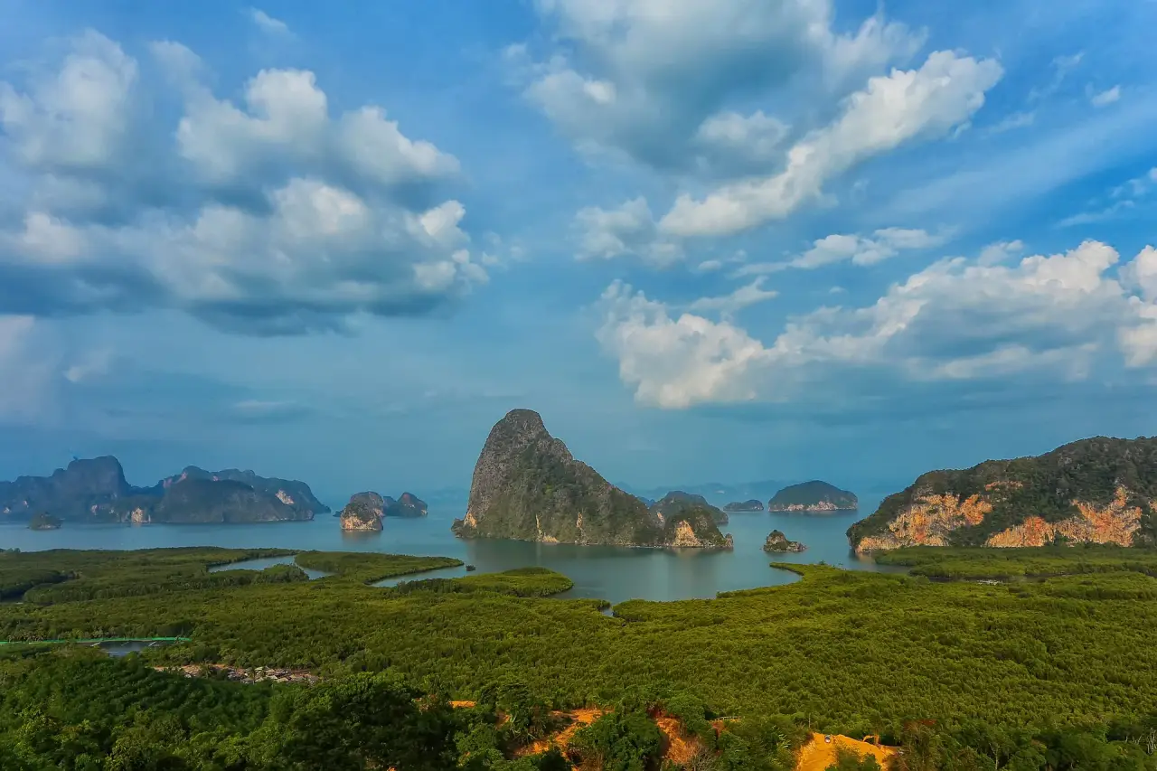 Islas de piedra caliza iluminadas por el sol de la bahía de Phang Nga más allá de los manglares verdes, vistas desde Samet Nangshe bajo un cielo azul nublado